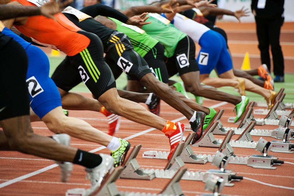 Start einer Sprintveranstaltung mit mehreren Athleten in Blockstartposition auf einer Laufbahn.